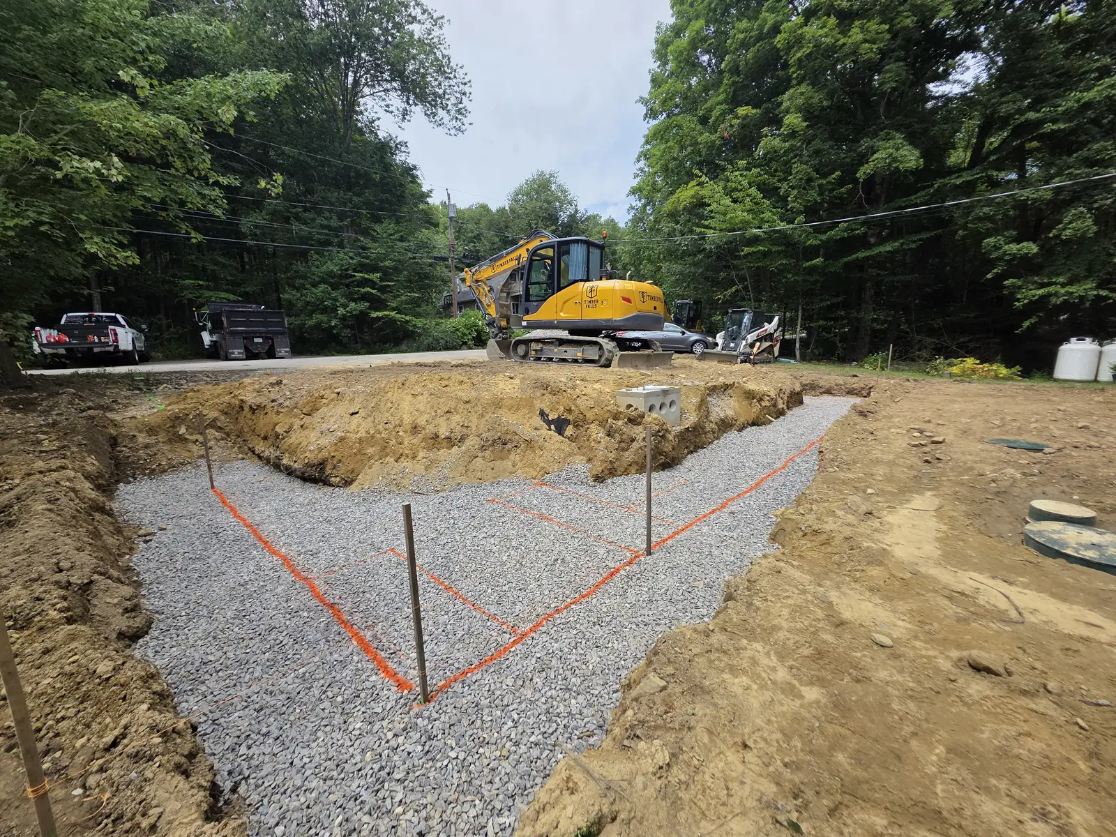 Excavated gravel base with layout markings and Timber Falls equipment behind it