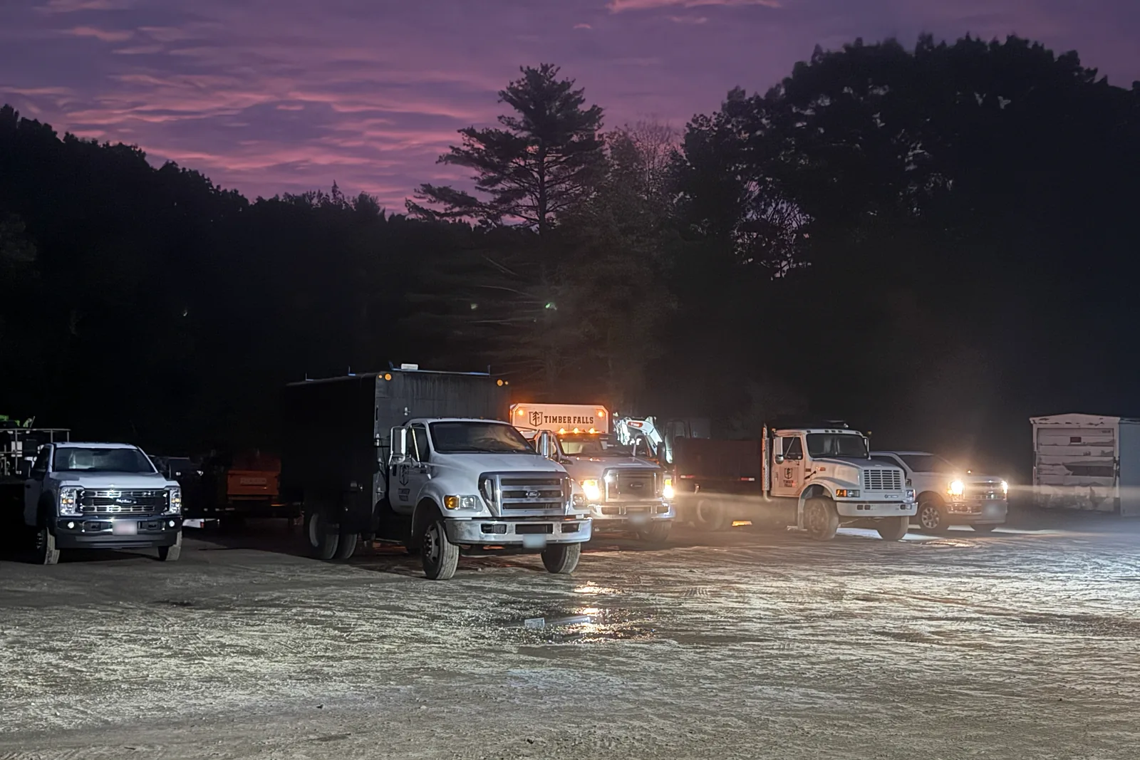 Timber Falls trucks and equipment at the yard beneath a dawn sky